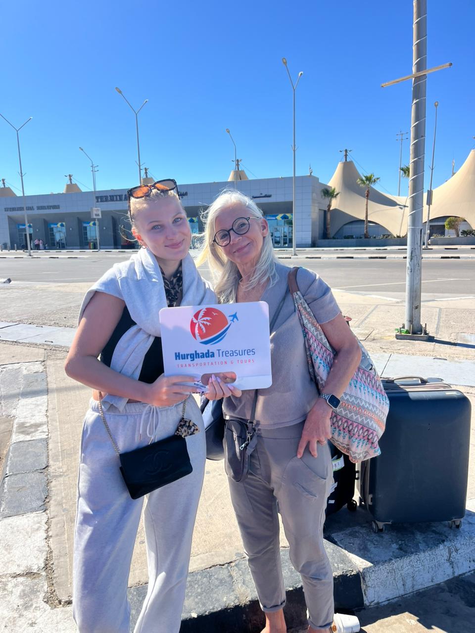 Two guests holding the Hurghada Treasures sign with their luggage at Hurghada International Airport Terminal